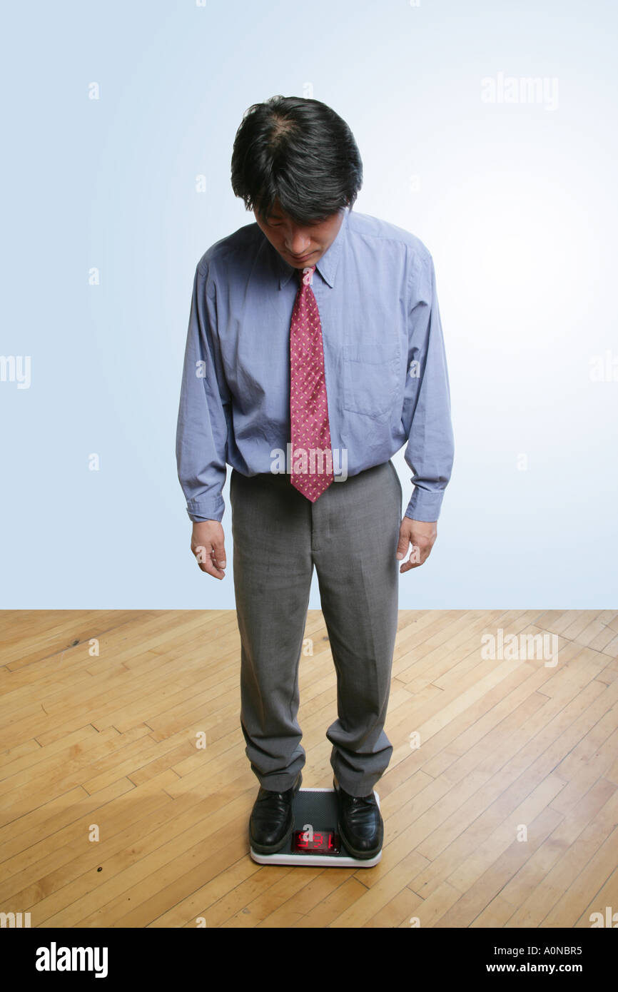 Asian man weighs himself using a bathroom scale, Stock Photo