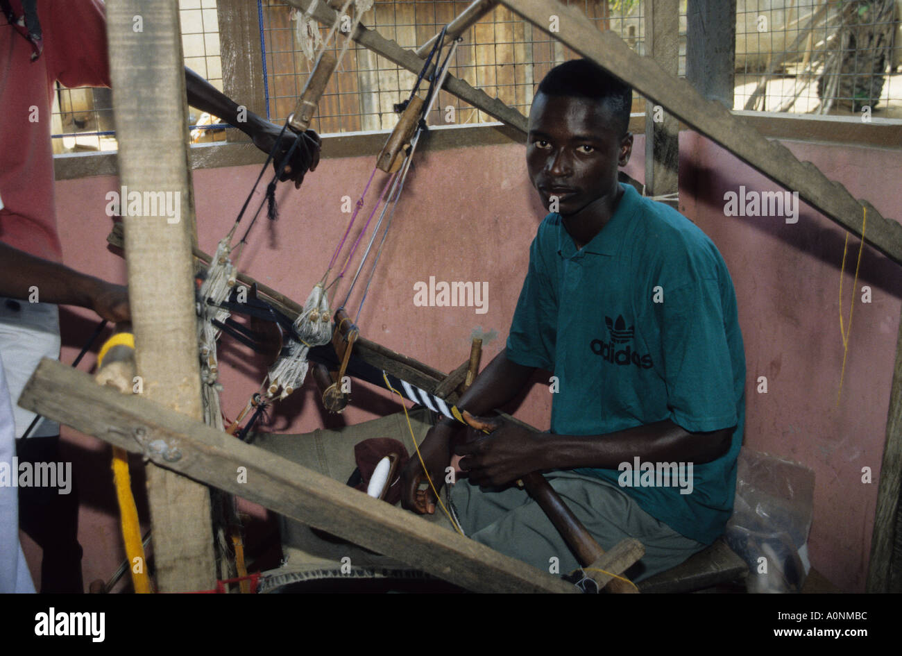 Young Kente cloth weaver wearing adidas T shirt at the loom in Kumasi  workshop Ghana Stock Photo - Alamy