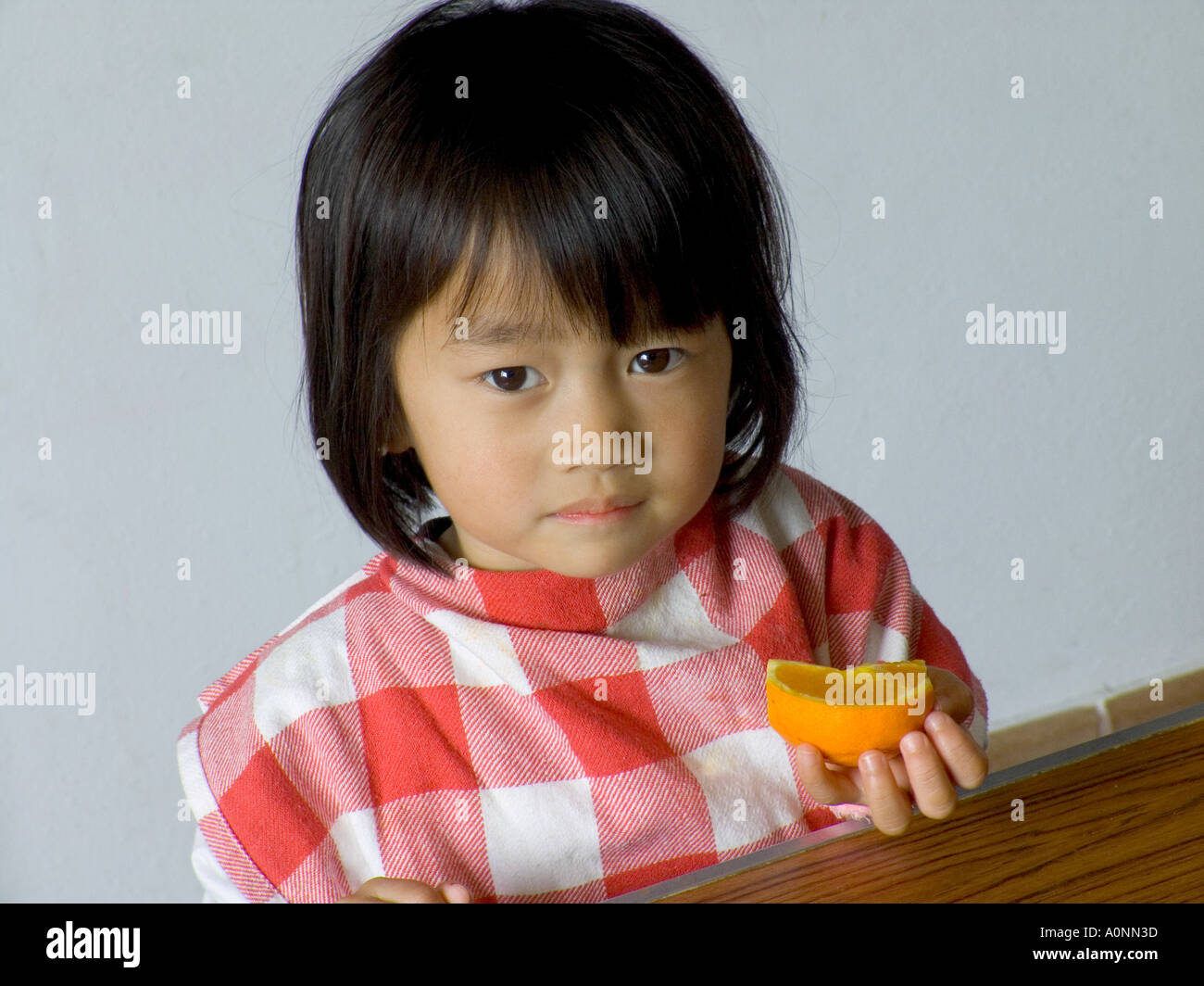Thoughtful young Oriental girl eating slice of orange in school canteen Stock Photo