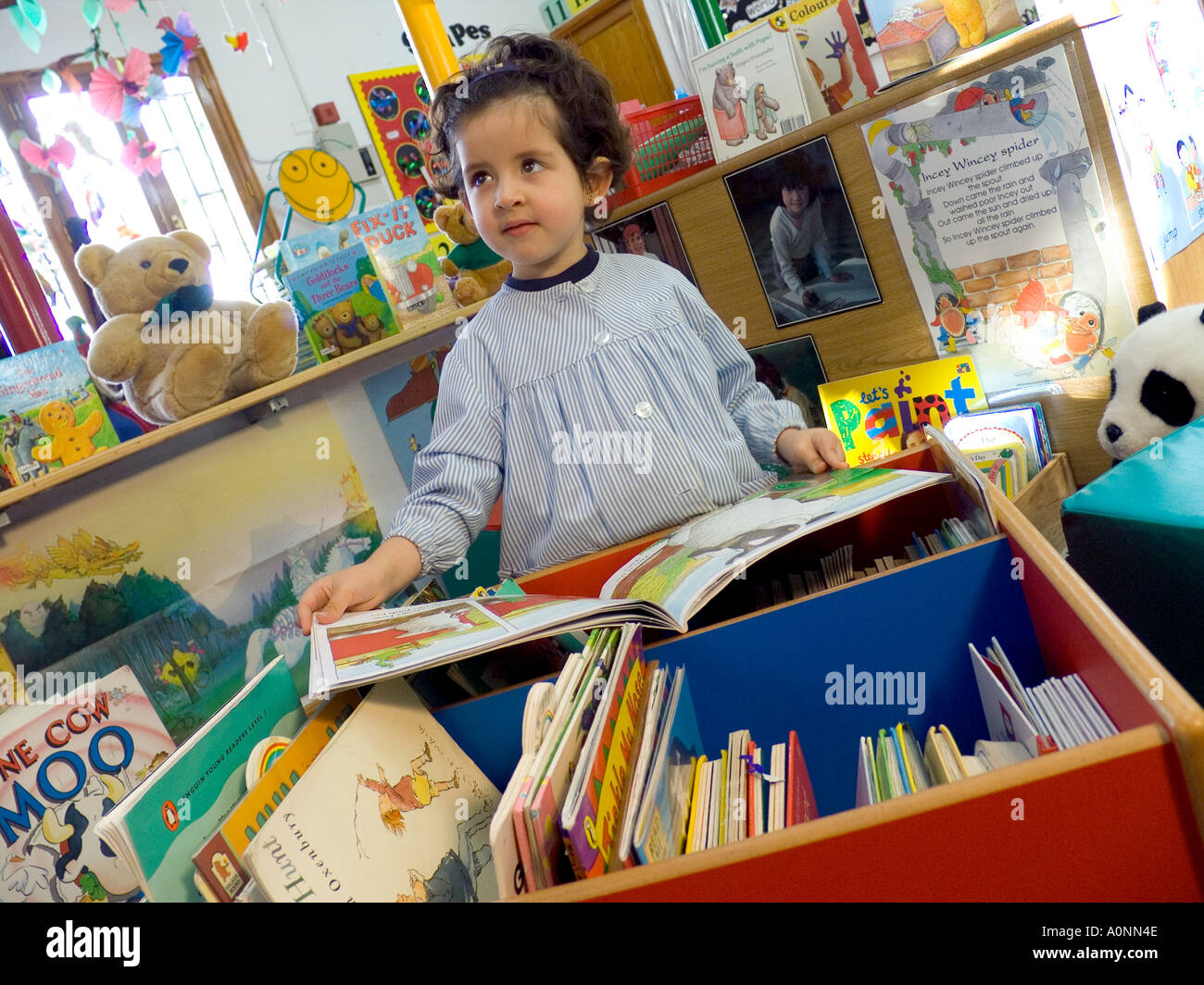 Young cute infant girl in play school learns to read from a selection of books in school kindergarten Stock Photo