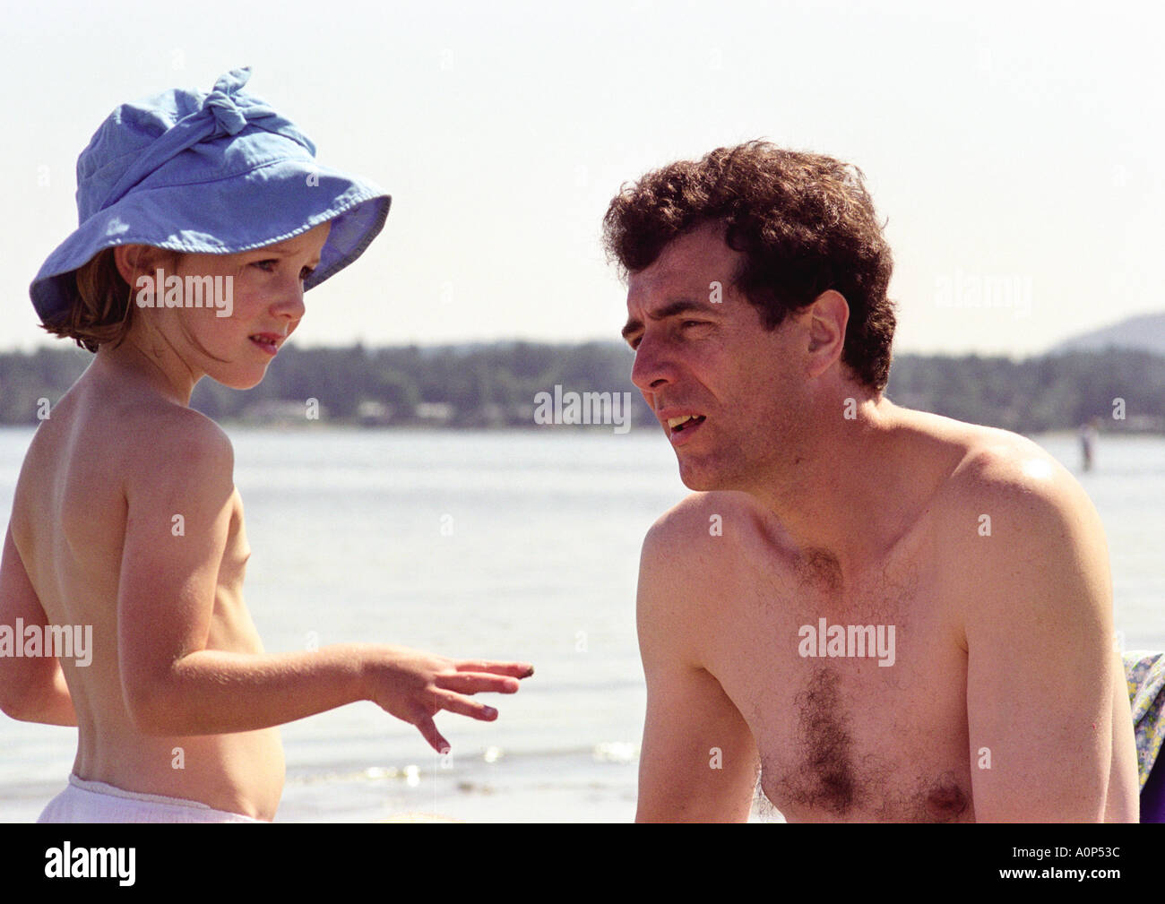 Father in conversation with young daughter while on holiday at the beach Stock Photo