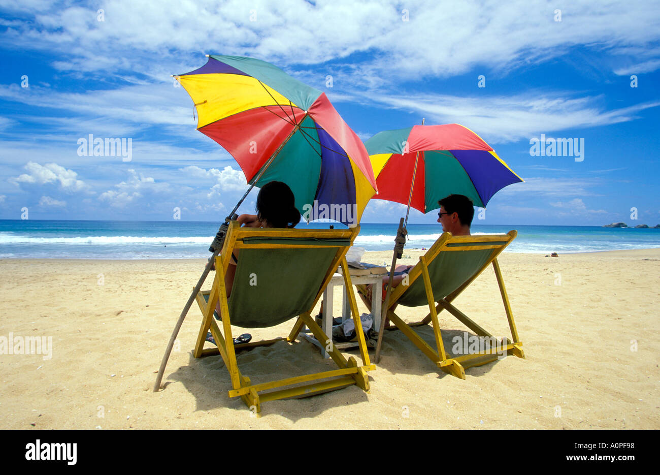 Couple sitting under colorful umbrellas Hikkaduwa beach, sri lanka Stock Photo