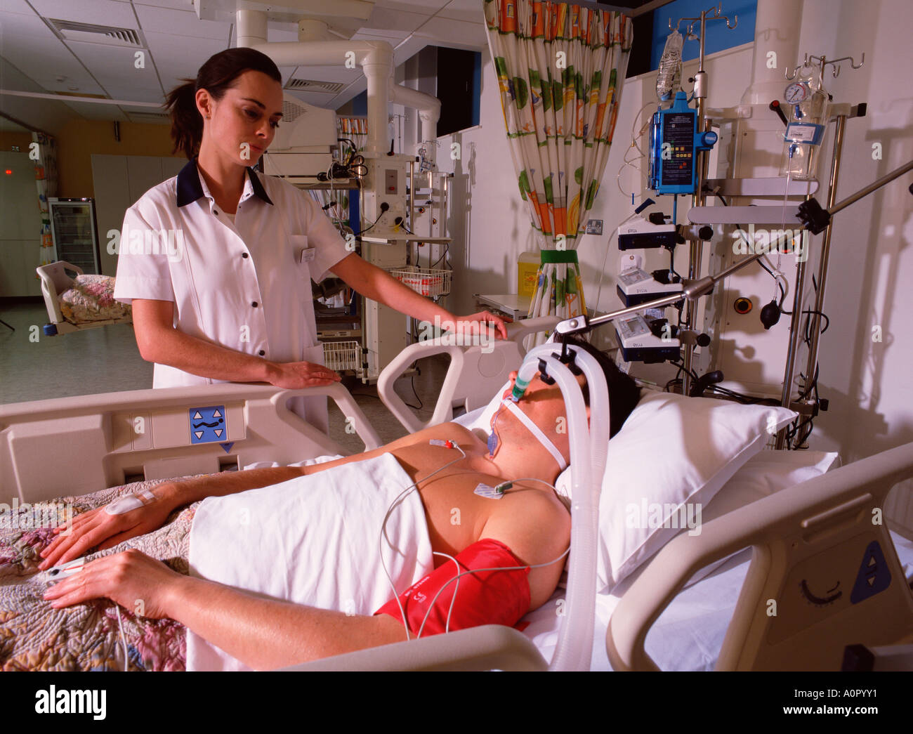 Hospital nurse tending to male patient in intensive care unit. Stock Photo