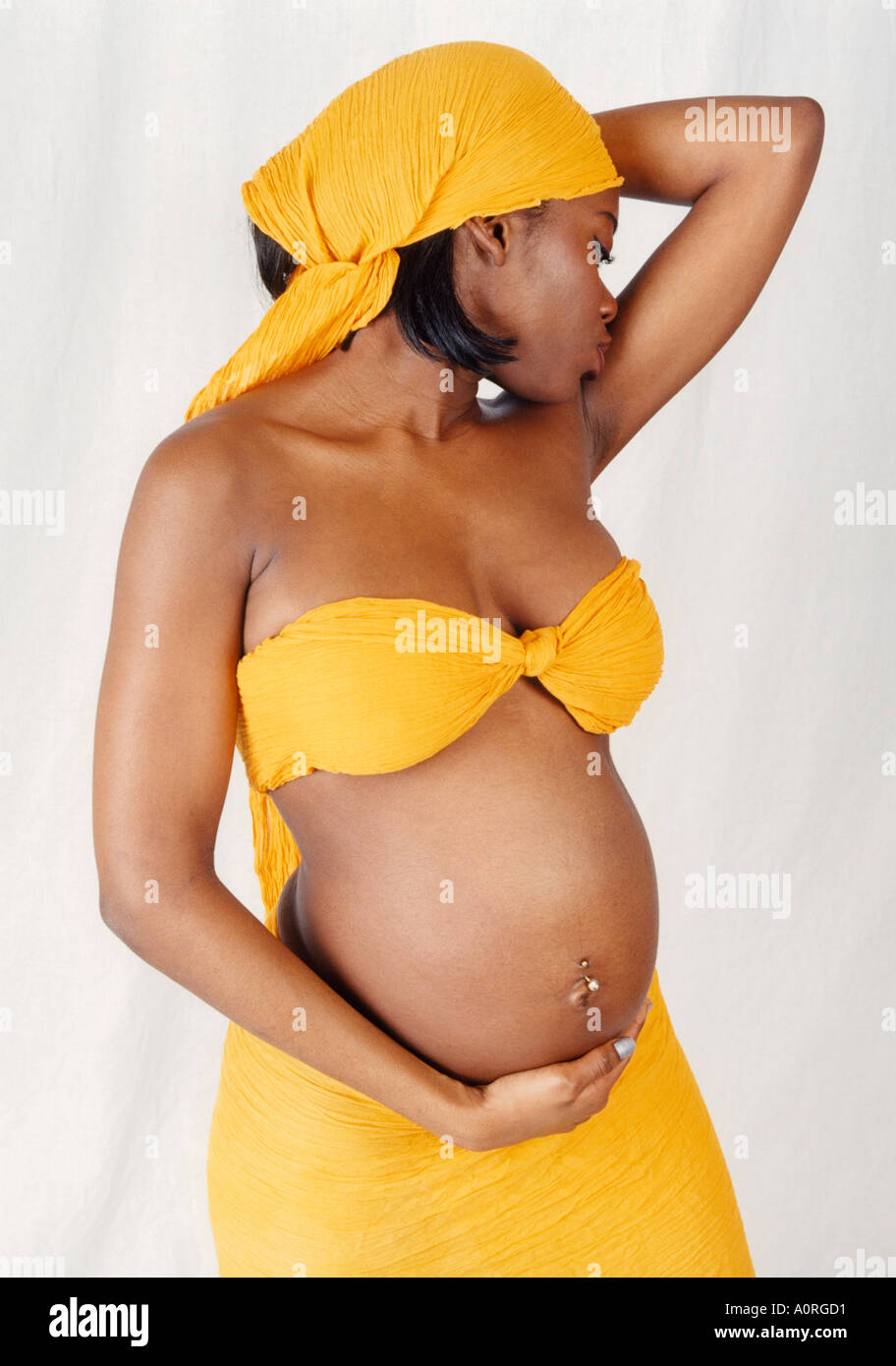 Portrait of a Black Pregnant Girl with a Yellow Headscarf Top and Skirt Holding Her Stomach Stock Photo