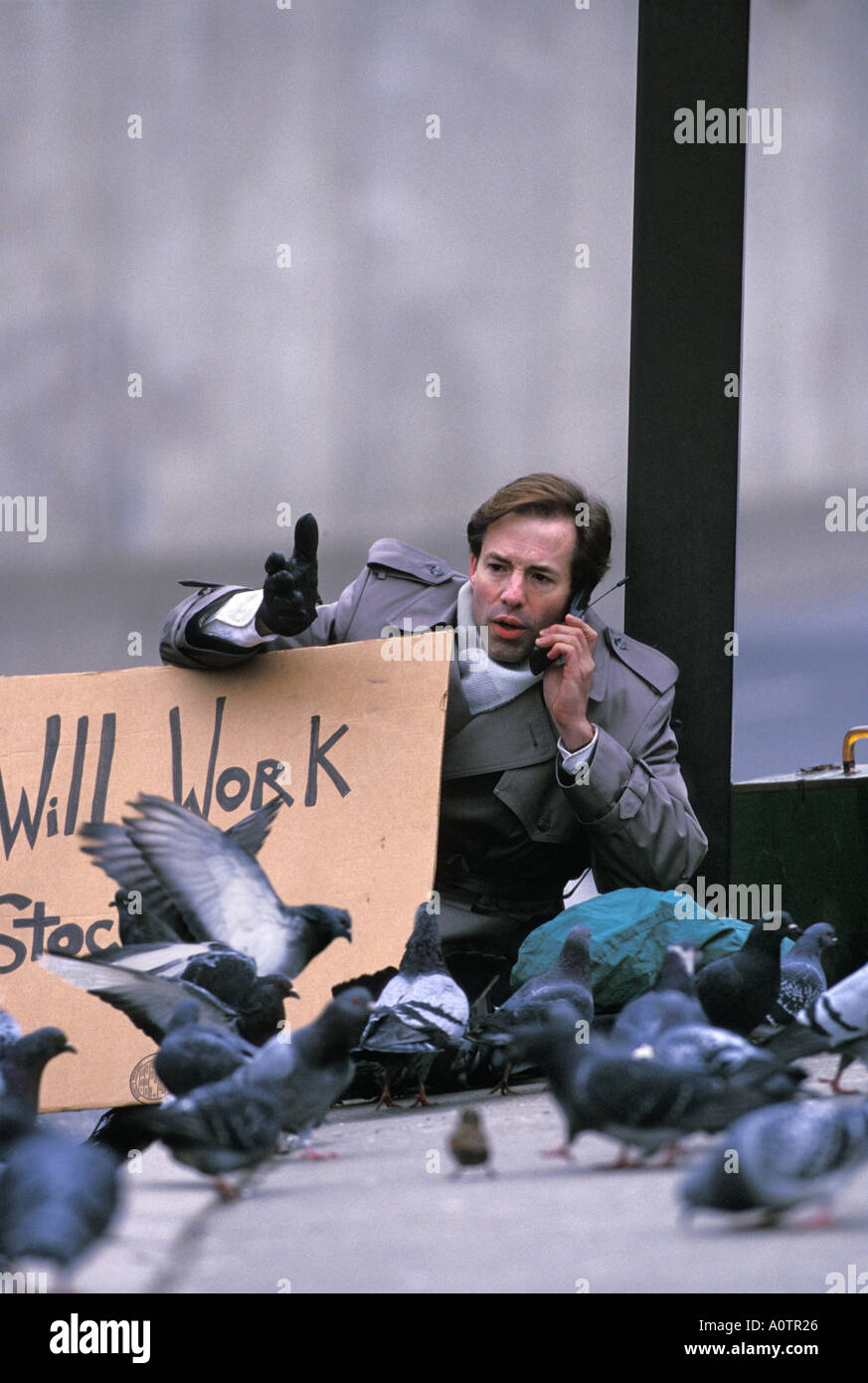 Humorous photo of an unemployed executive in the street surrounded by pigeons while holding a sign Stock Photo