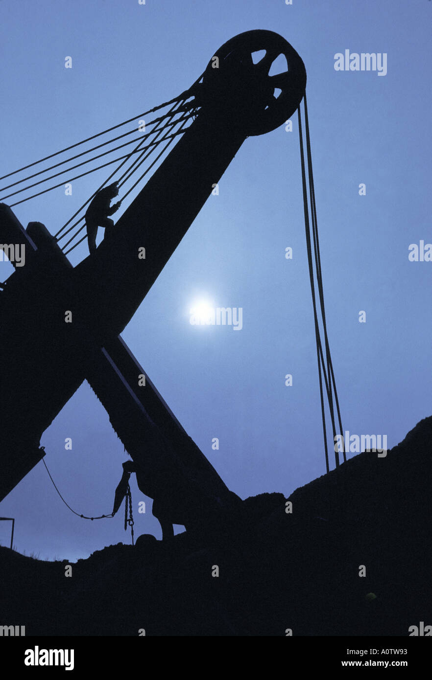 silhouette of a workmen on top of an oversized dragline shovel At an open pit mine Stock Photo