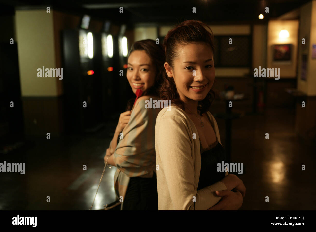 Portrait of two young women standing back to back and smiling in a ...