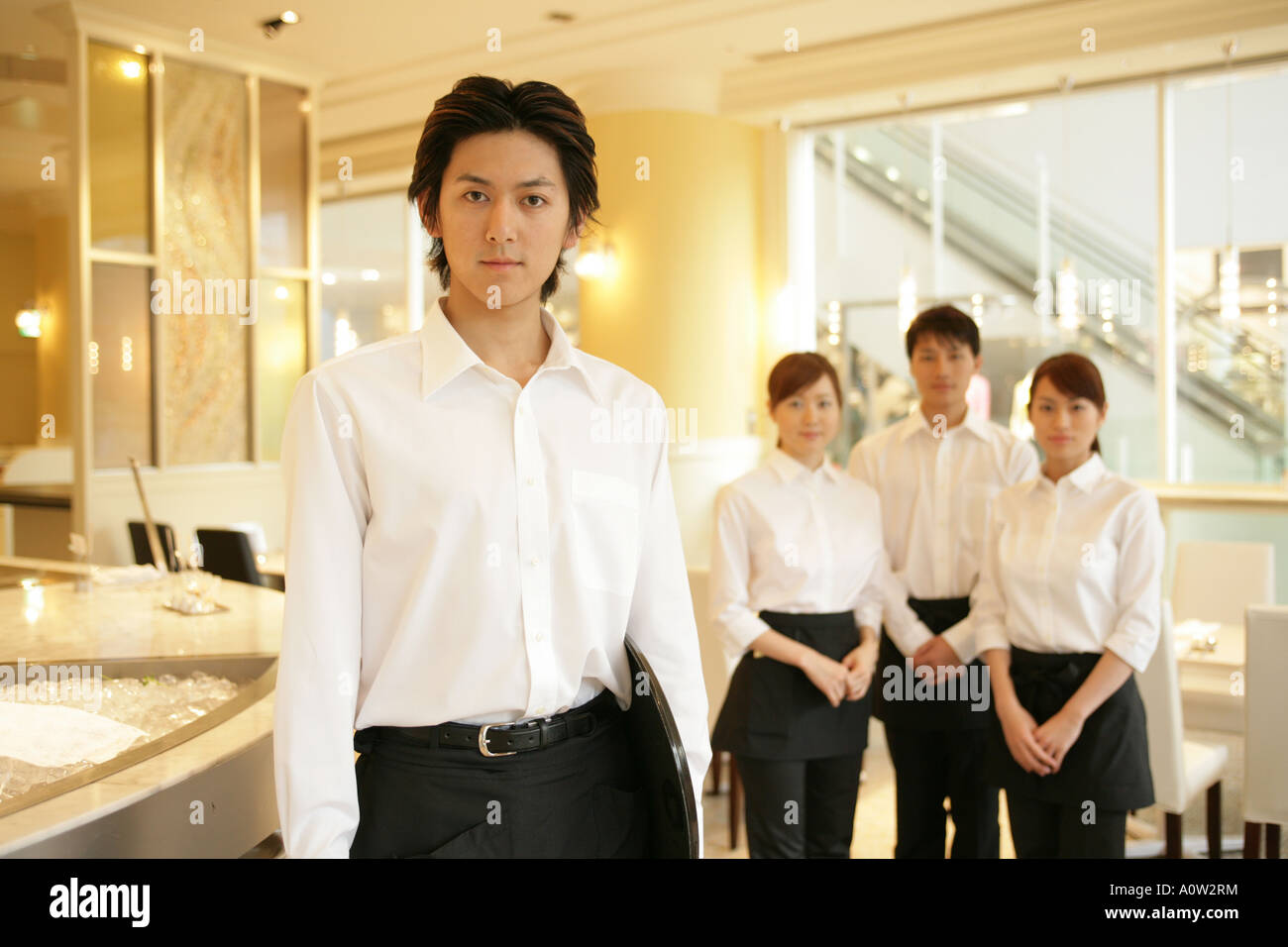 Portrait of two waiters and two waitresses standing in a restaurant ...