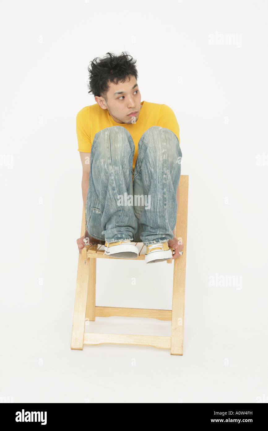 Young man balancing on a wooden chair and looking away Stock Photo