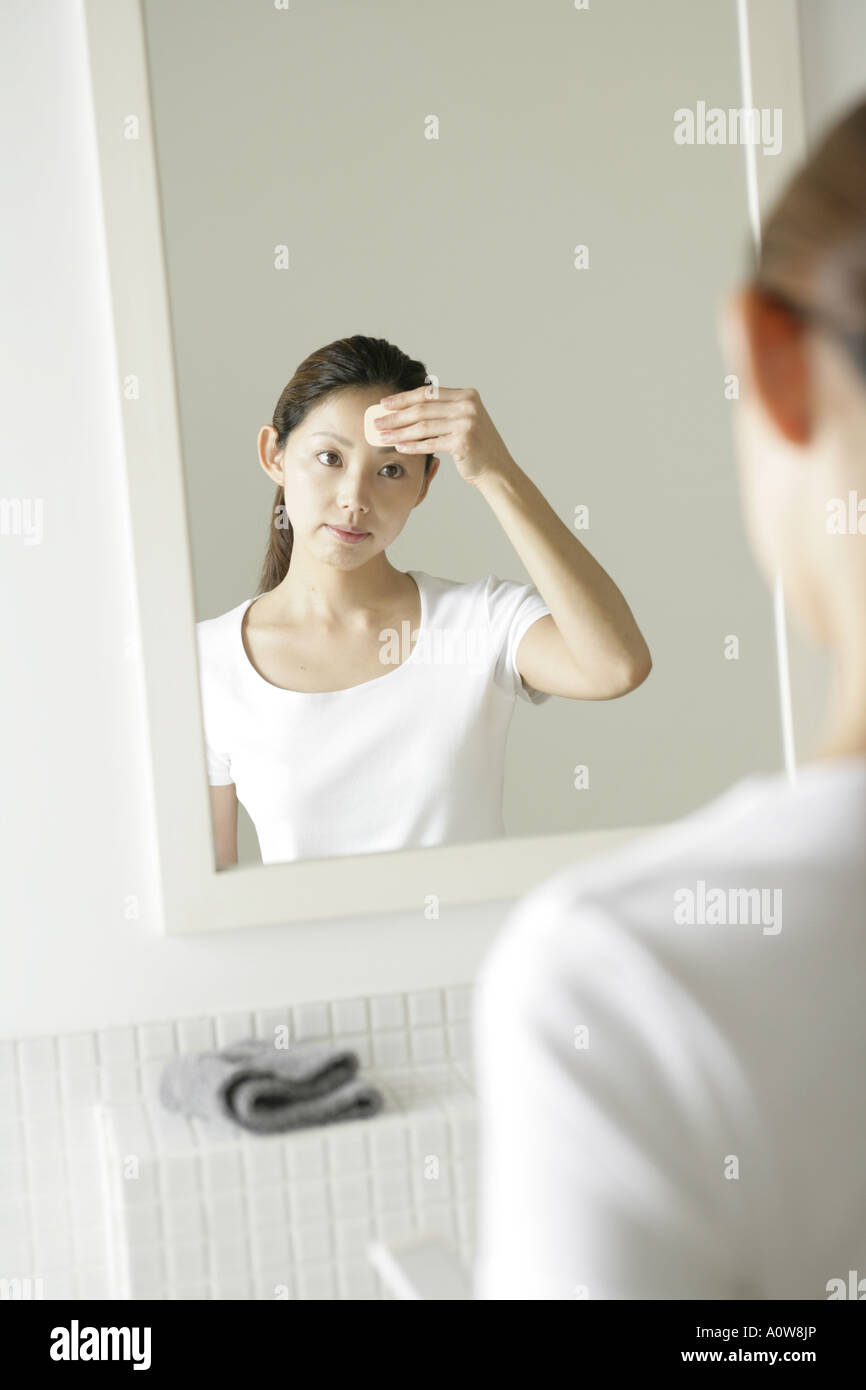 Reflection of a young woman in the mirror applying face powder on her ...