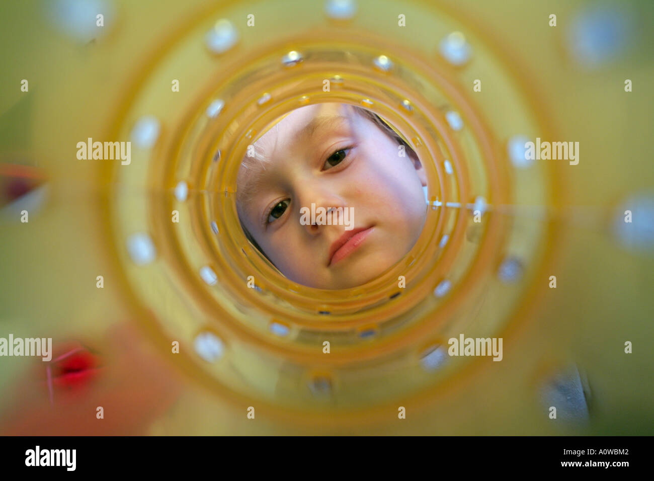 Young girl looking through her yellow plastic toy. Stock Photo