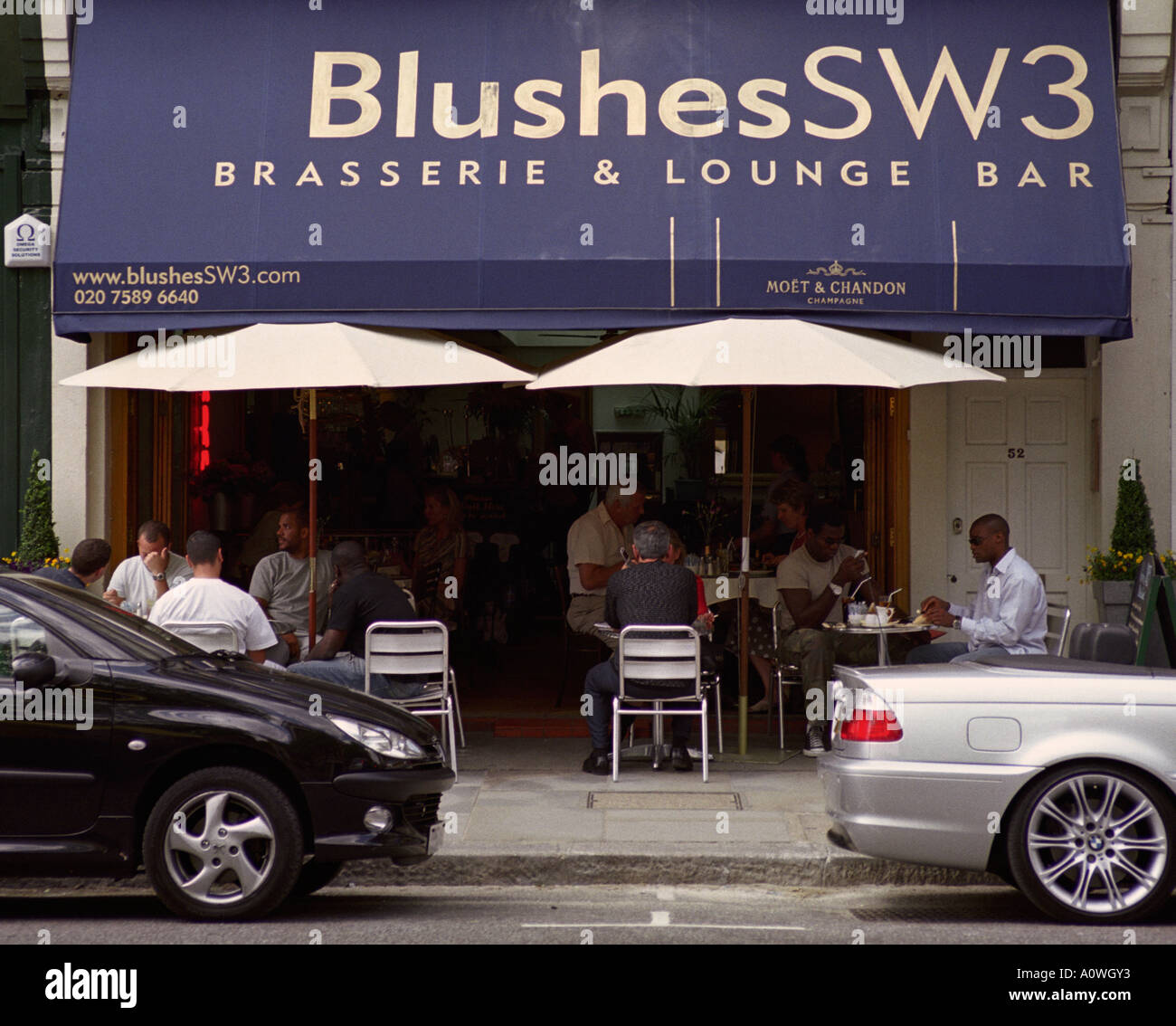 ENGLAND LONDON Cafe society framed between shiny sports cars on the King s Road in affluent Chelsea Stock Photo