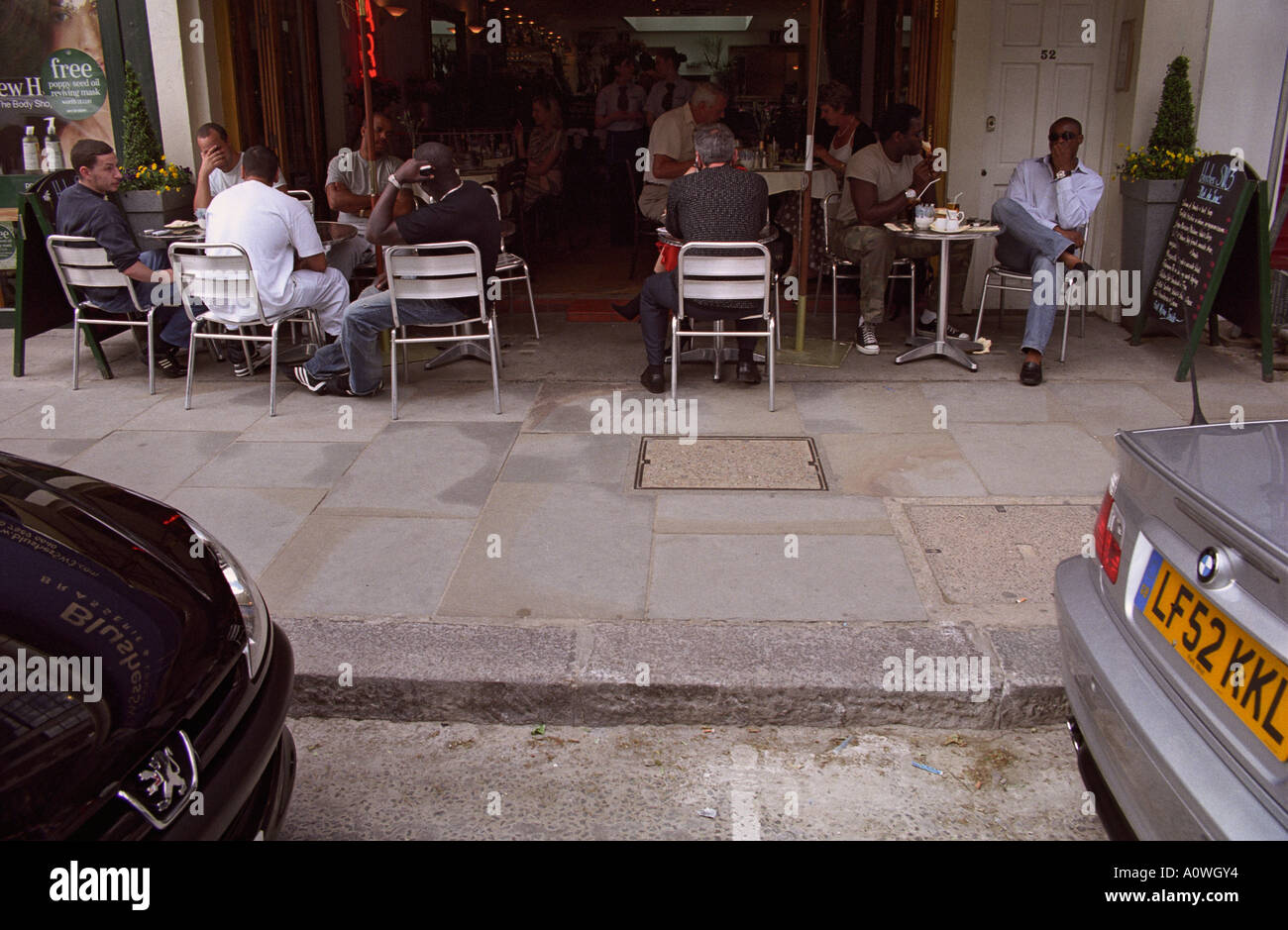 ENGLAND LONDON Cafe society framed between shiny new sports cars on the King s Road in affluent Chelsea Stock Photo