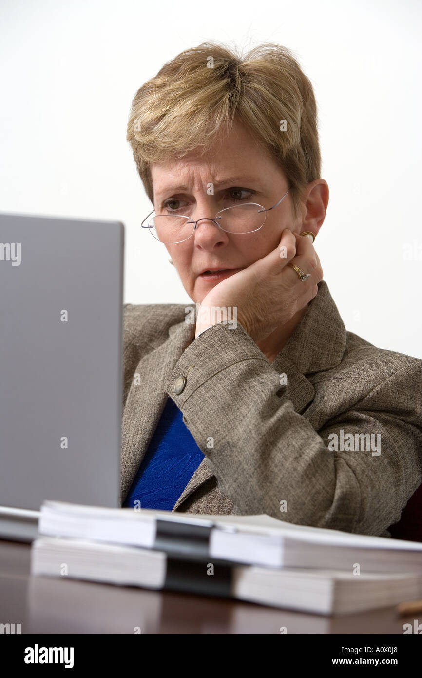Female executive working on portable computer while surrounded by a mound of paperwork in office conference room Stock Photo