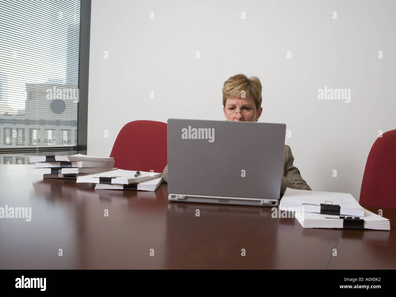 Female executive working on portable computer while surrounded by a mound of paperwork in office conference room Stock Photo