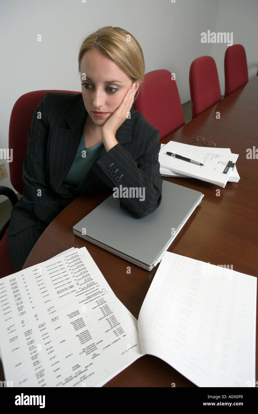 female executive office worker ponders over workload and paperwork in corporate conference room Stock Photo