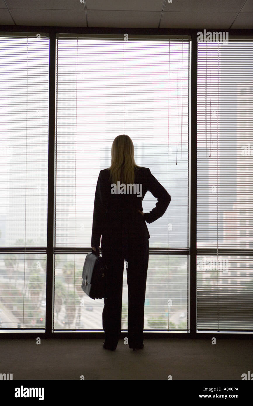 female executive looks out at downtown Los Angeles, CA skyline from new office space Stock Photo