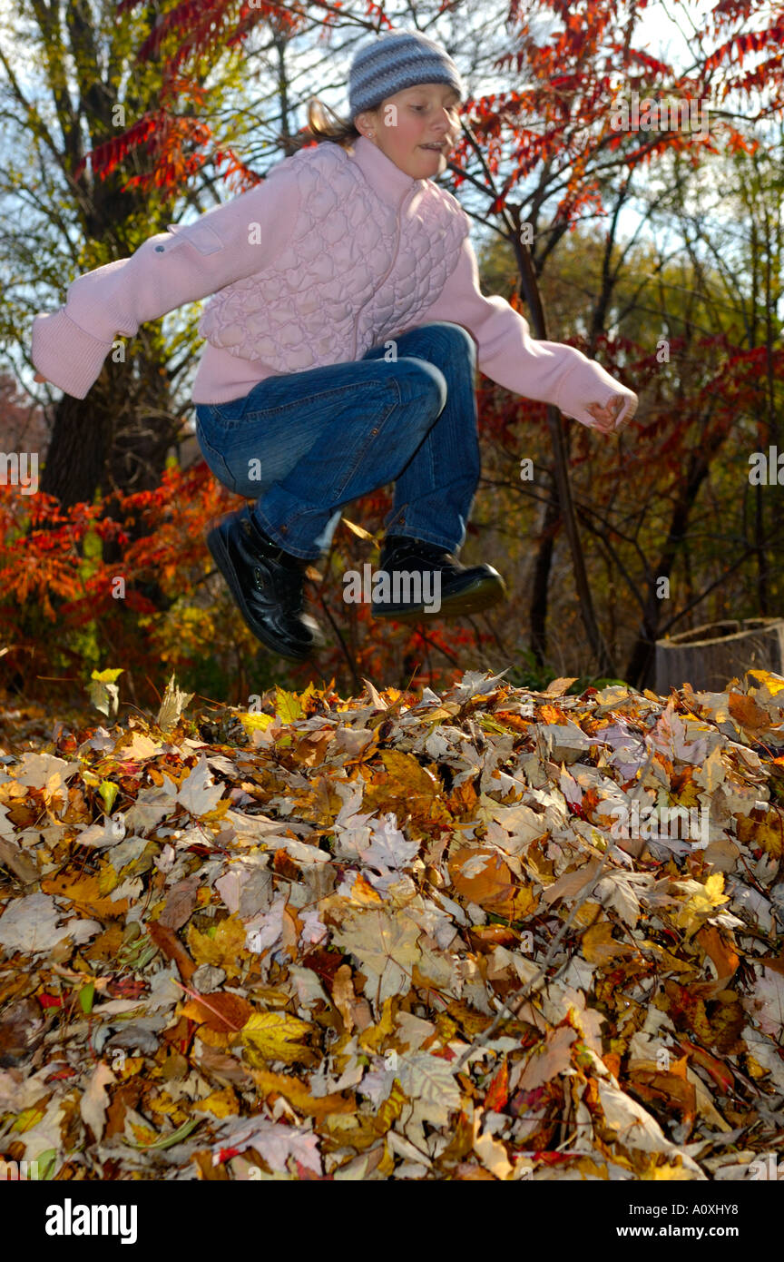 Girl running and jumping into a pile of leaves in the Fall Stock Photo