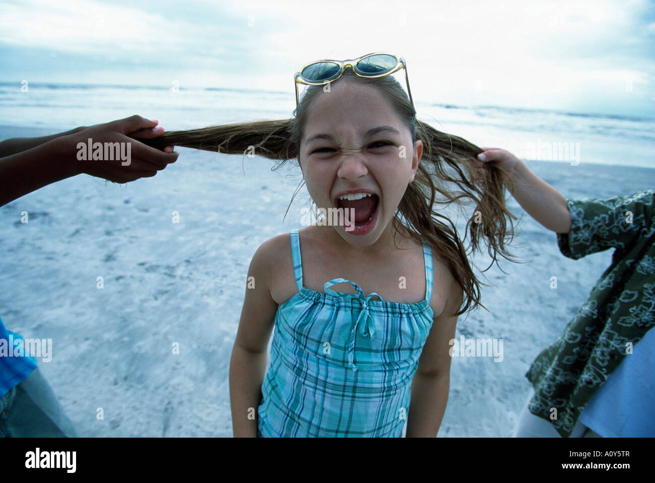 Closeup of two people pulling a girl's hair on the beach Stock Photo