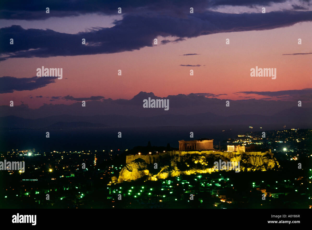 A darkening pink sky at dusk settles over the ruins of the Acropolis dating back to the 5th c BC and overlooking the twinkling lights of Athens from a 300 feet high rock Stock Photo