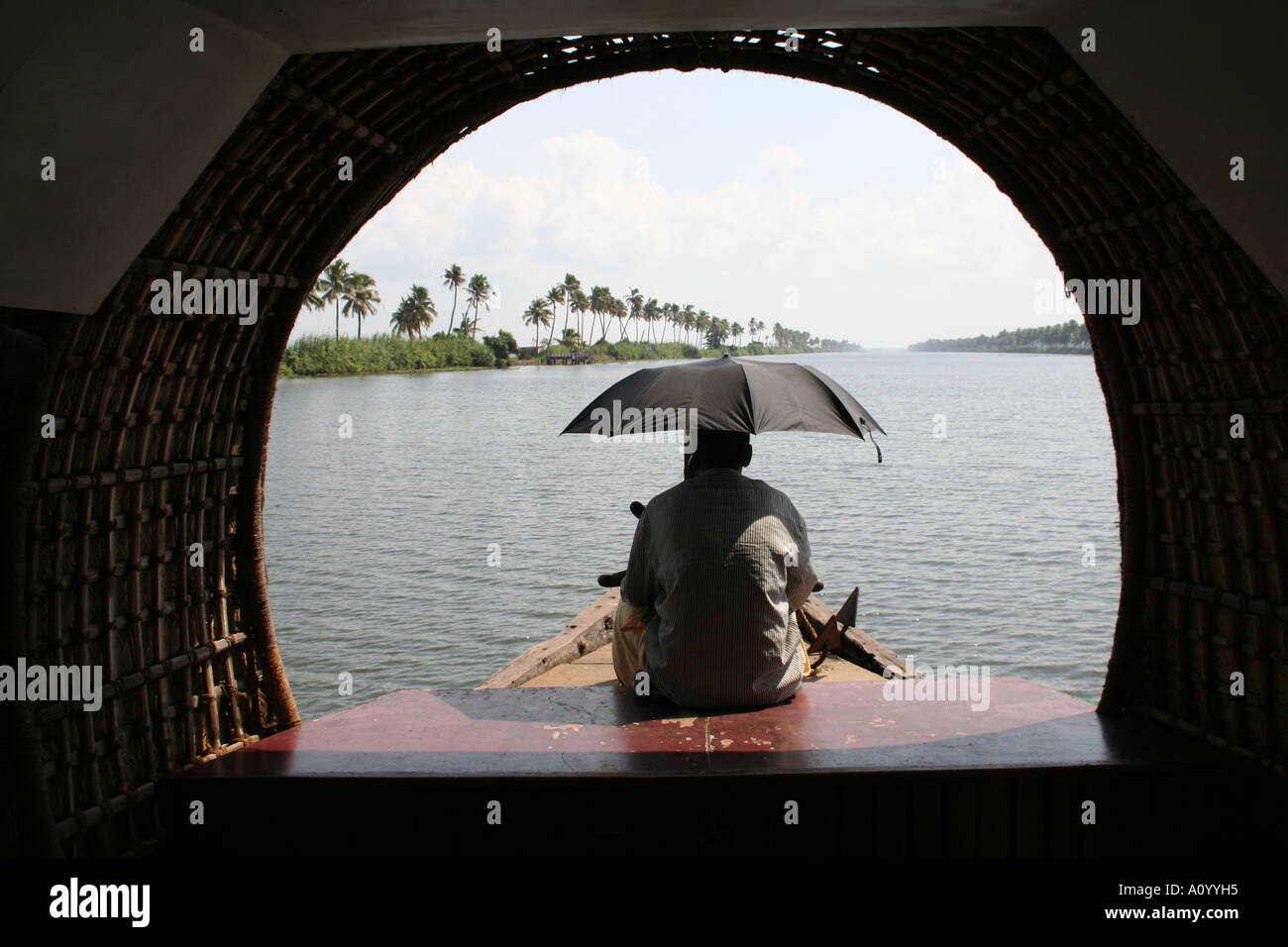 Man with umbrella steering a house boat on the backwaters of kerala in india Stock Photo