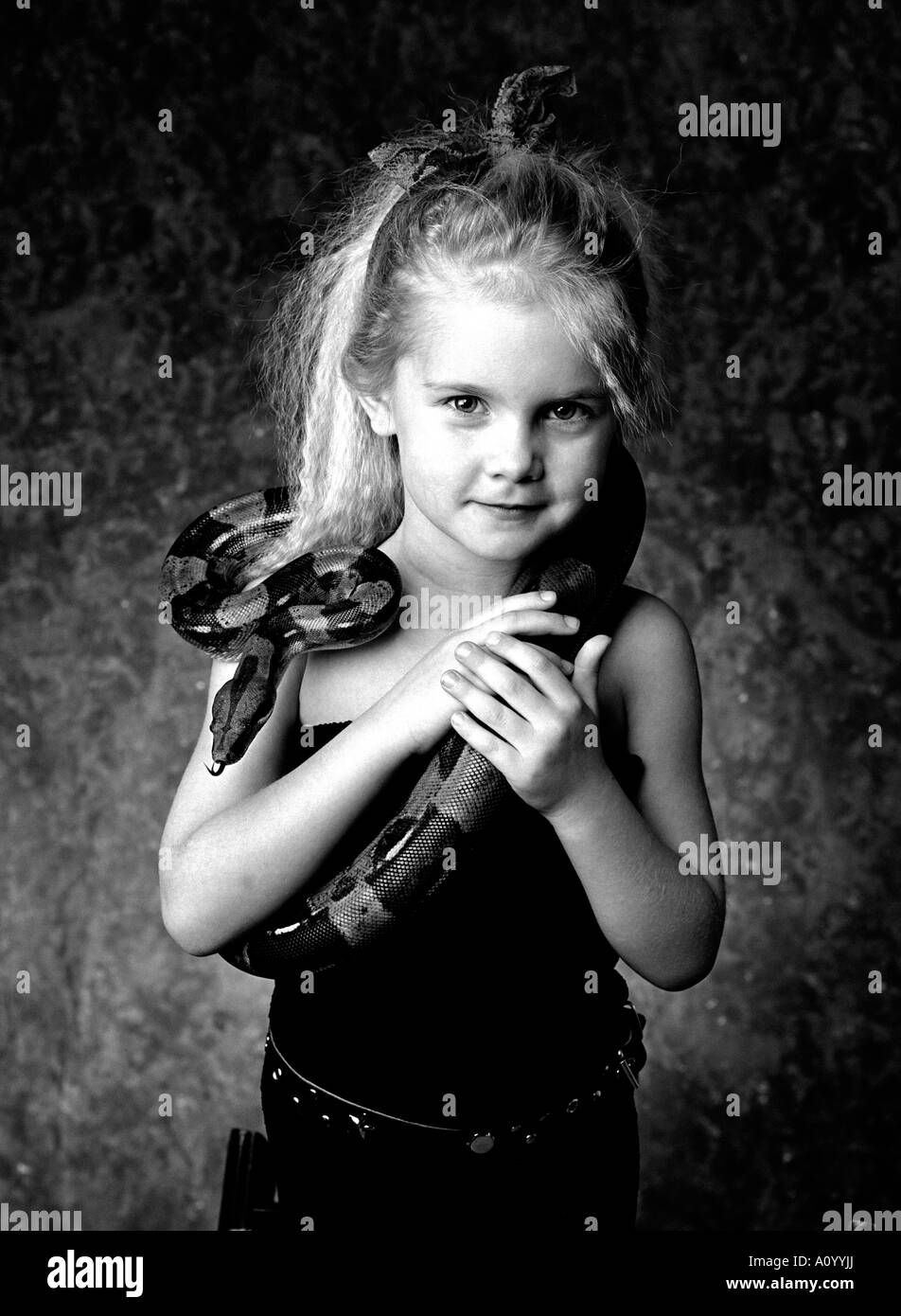 Little girl about five years oldwith long blond hair and mischievous smile holding pet snake. B/W. Stock Photo