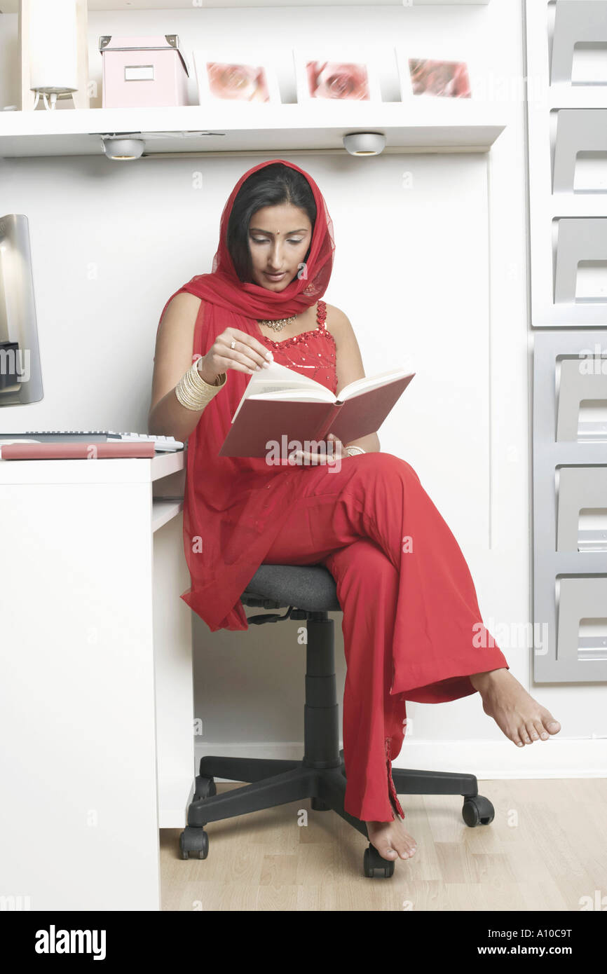 Young woman sitting on a chair and reading a book Stock Photo - Alamy