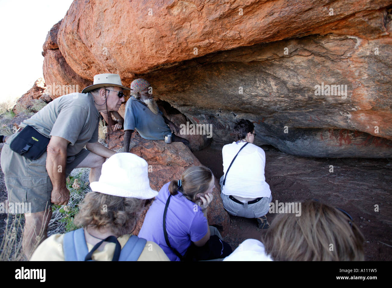 Holidaymakers look at ancient aboriginal cave paintings with a local aborigine guide, Anangu Pitjantjara lands, South Australia Stock Photo