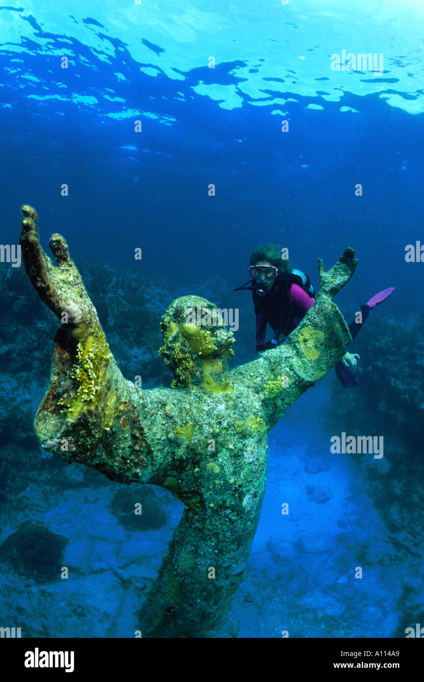 A FEMALE SCUBA DIVER AND THE STATUE OF CHRIST OF THE DEEP ON A CORAL