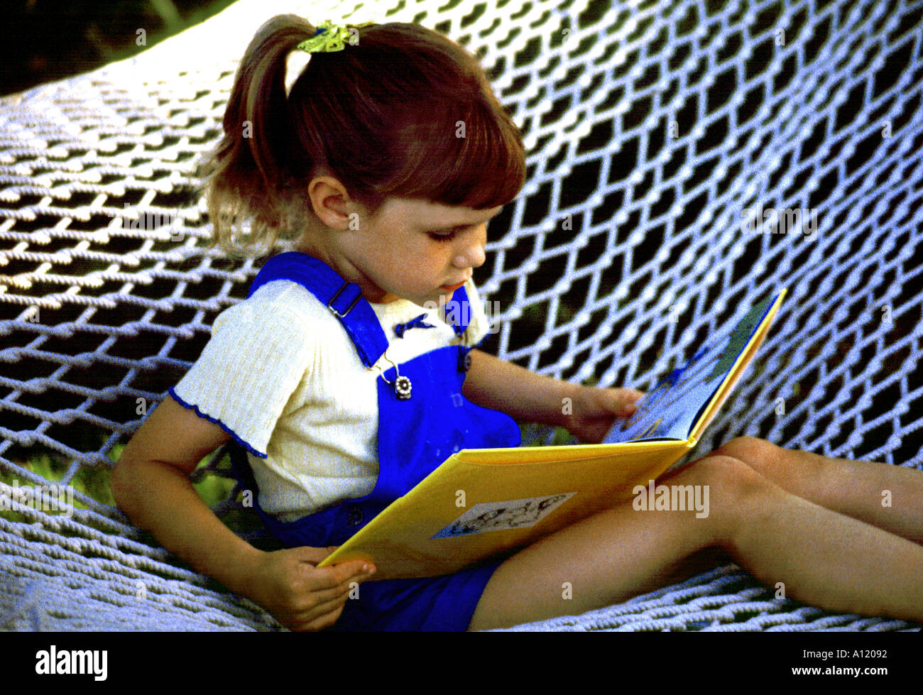 Young girl in hammock reading book Stock Photo - Alamy