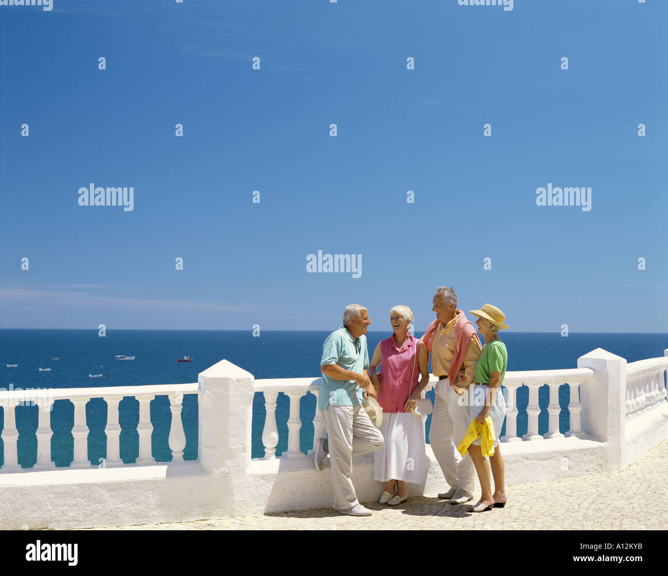 retired age couples leaning on balustrades and chatting with sea in background Stock Photo