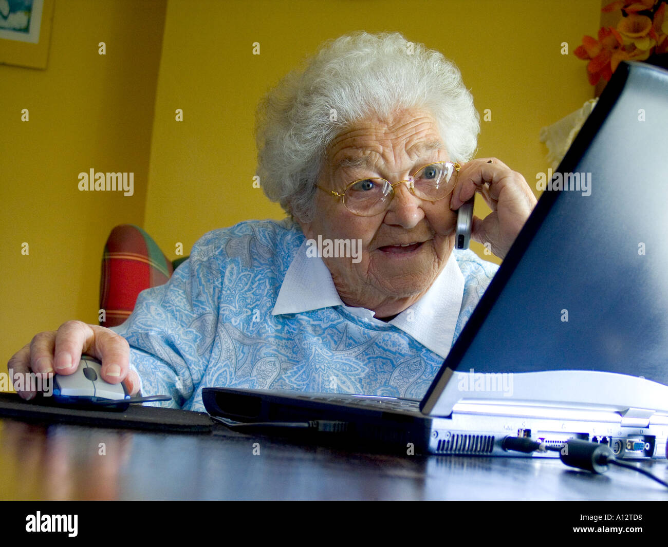 Computer screen cell phone elderly lively senior lady is fascinated by her laptop computer screen whilst talking on her mobile cell phone Stock Photo