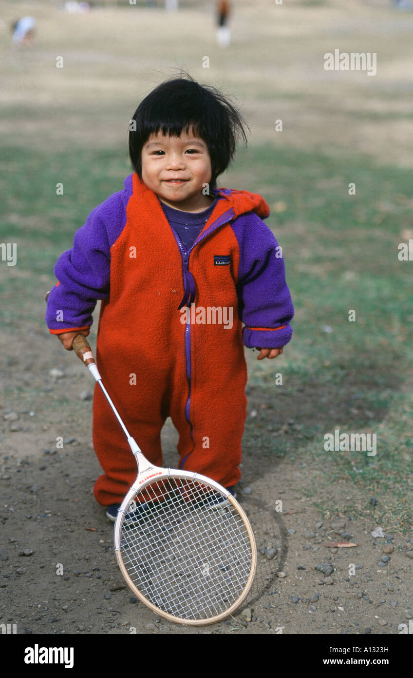 A small Japanese boy holds a badminton racquet in a Tokyo park, Japan Stock Photo
