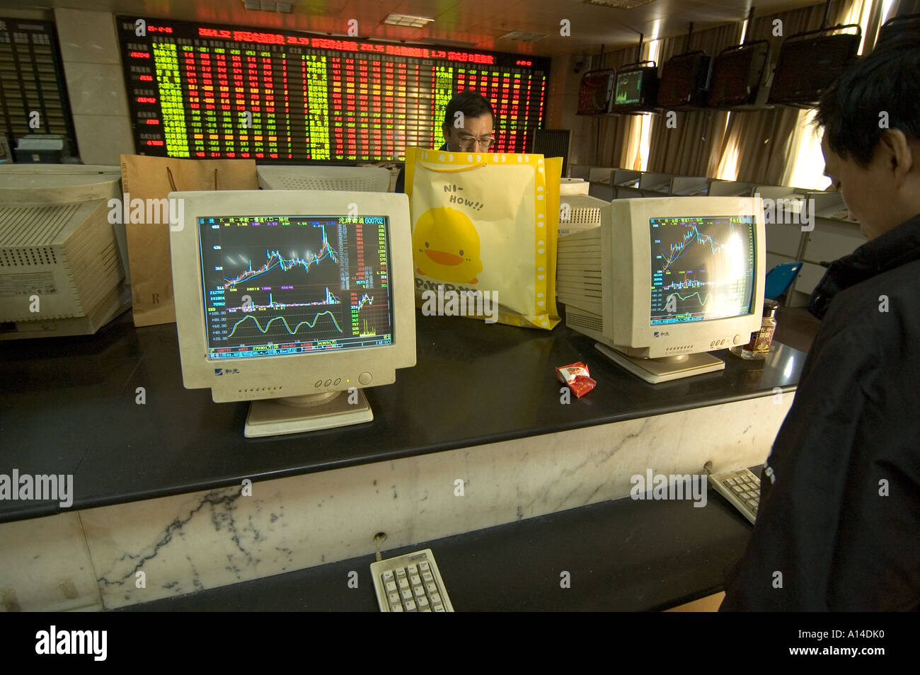 People trading in a Shanghai Stock market exchange branch open to the public, with screens displaying charts of share prices. Stock Photo