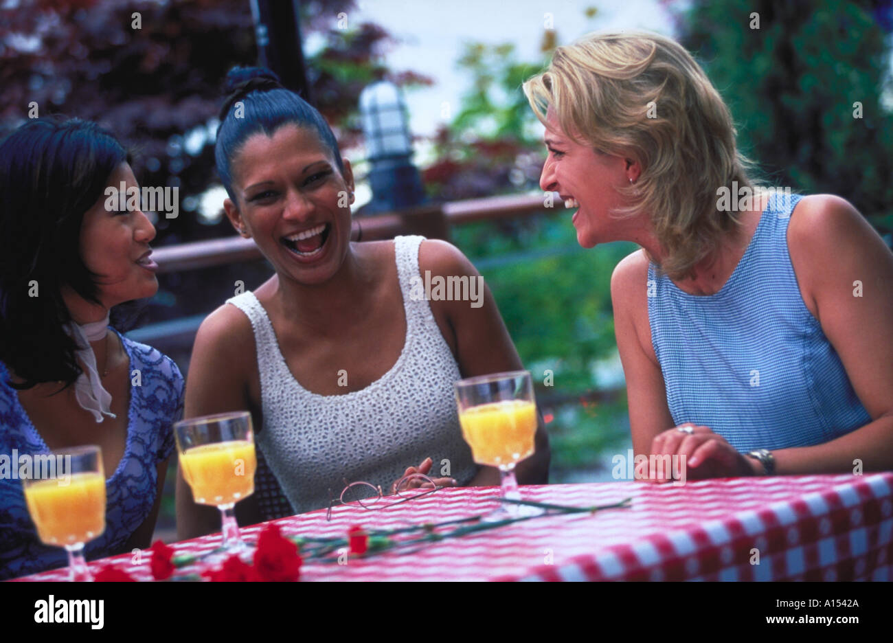 Three women sitting outside at a table with drinks laughing Stock Photo