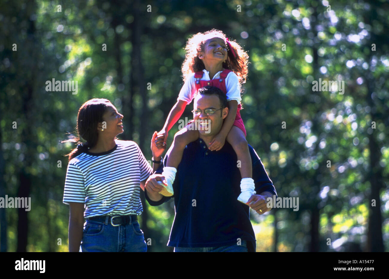 An African American family walking in the park The daughter is riding on her dad shoulders Stock Photo