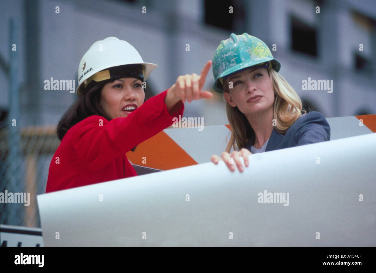 Two female architects holding blue prints and wearing hardhats while inspecting a work site Stock Photo