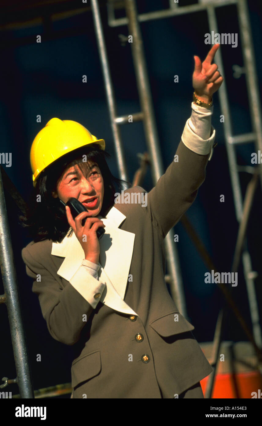 An Asian woman wearing a hard hat supervises on a construction site Stock Photo