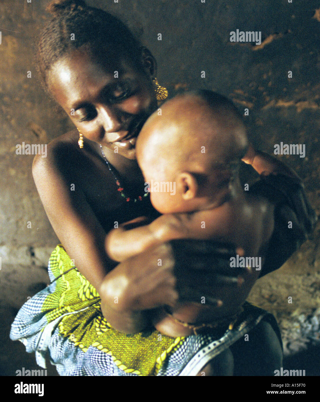 Halima Balde holds her new born baby inside the dimly lit mud hut in the Muslim Fulani village of Dempel Jumpora in Guinea Stock Photo