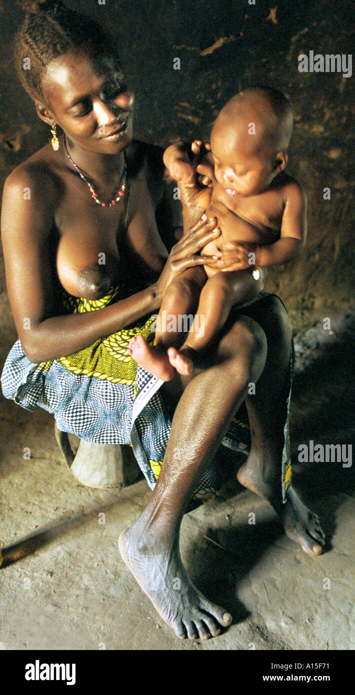 Halima Balde feeds her new born baby inside the dimly lit mud hut in the Muslim Fulani village of Dempel Jumpora in Guinea Stock Photo