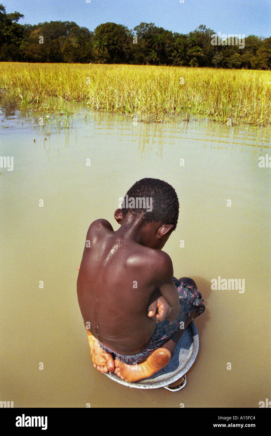 Tcherno Balde takes a break from the heat by resting in the water while his mother cleans pots and pans in the Muslim Fulani Stock Photo