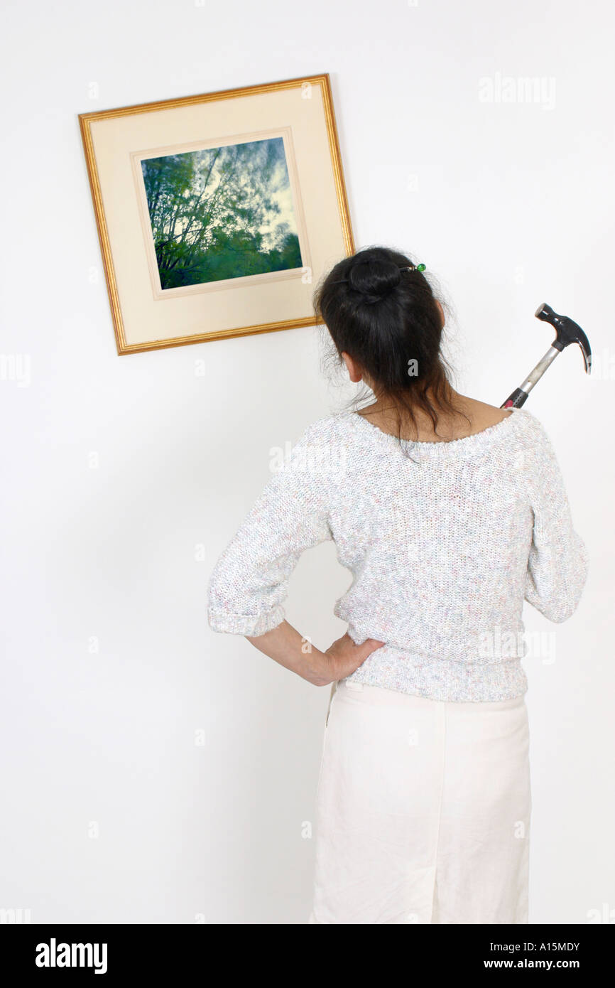 Rear View Of Woman Holding Hammer Looking At Crooked Picture On Wall rear-view-of-woman-holding-hammer-looking-at-crooked-picture-on-wall