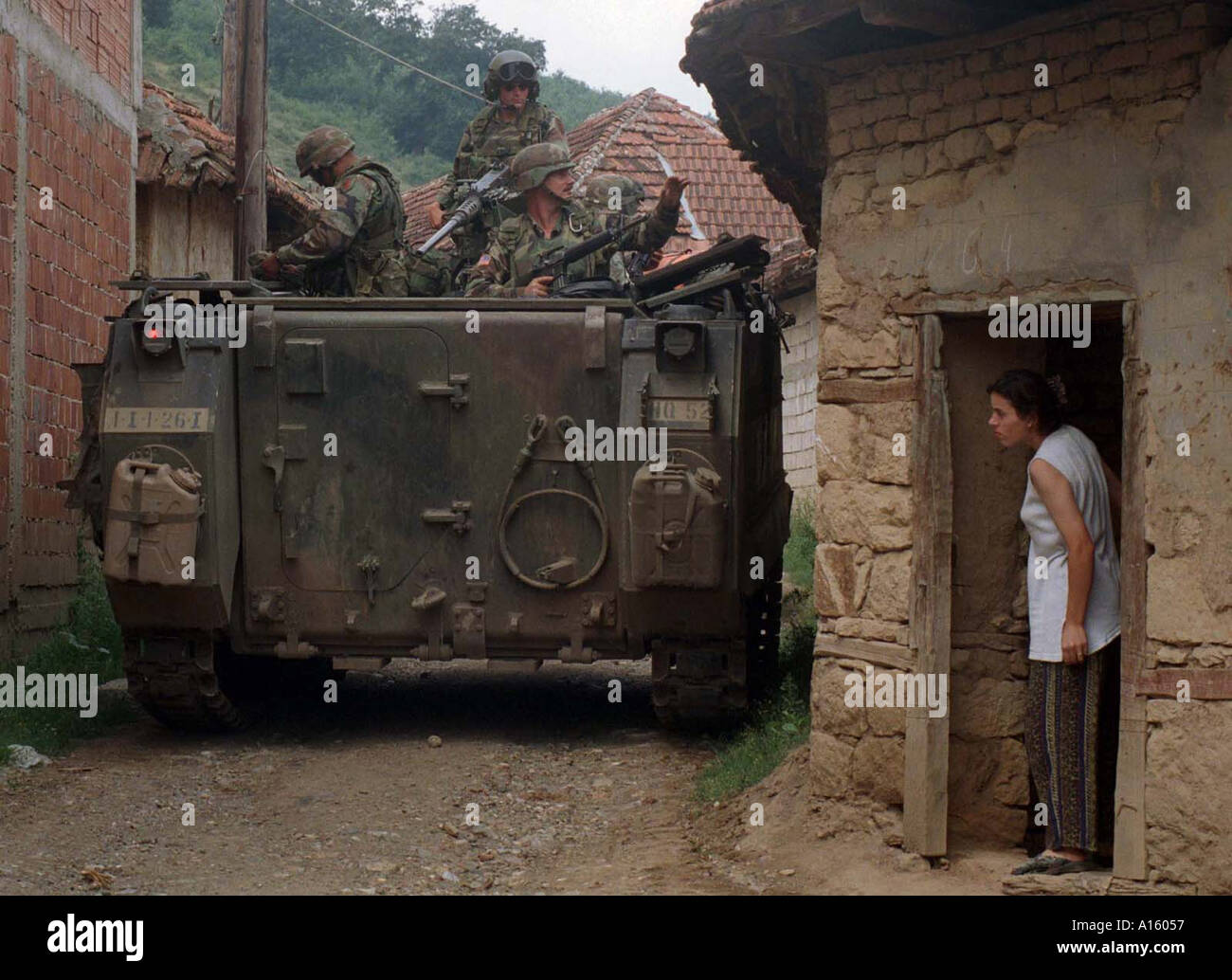 An ethnic Albanian watches American troops patrol through her village near Kololec where 2 Serbs were allegedly shot Monday Stock Photo