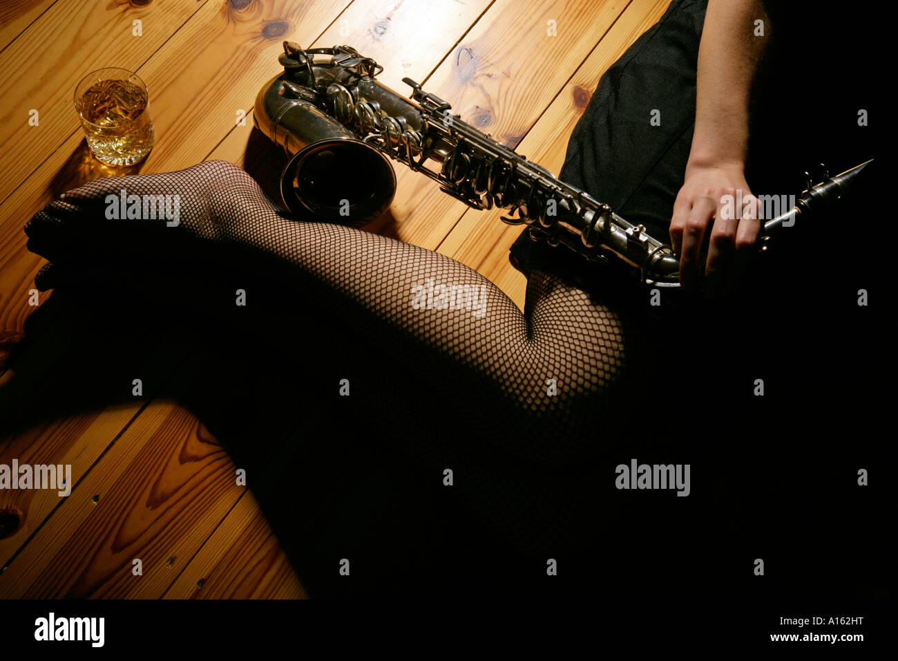 late night or low light image of a pair of female womans legs in fishnet  stockings alongside an alto sax and a glass of whisky Stock Photo