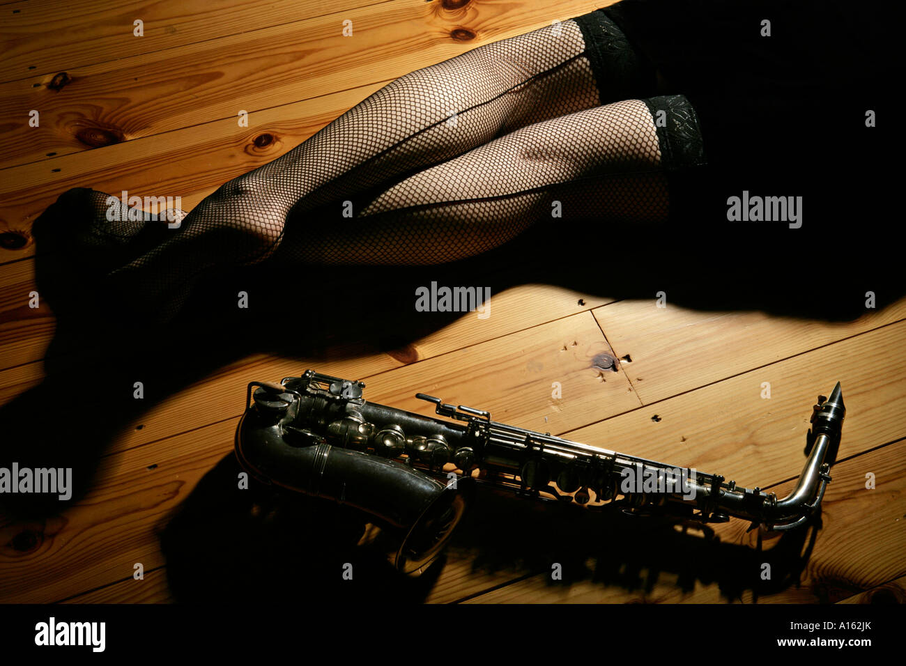late night or low light image of a pair of female womans legs in fishnet  stockings alongside an alto sax and a glass of whisky Stock Photo