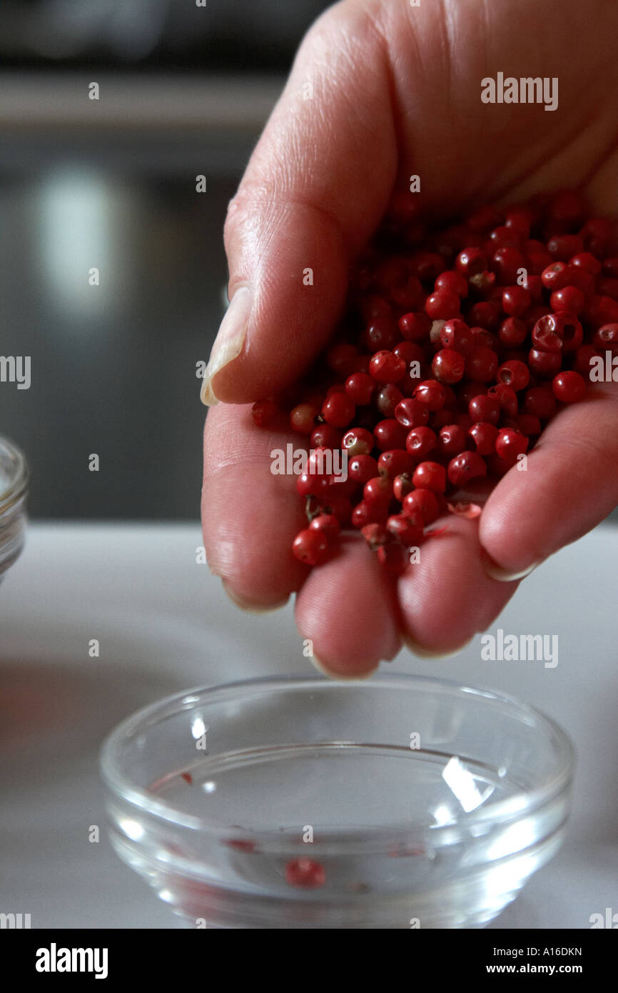 Pink peppercorns pour from a chef's hand into a small glass bowl. Stock Photo