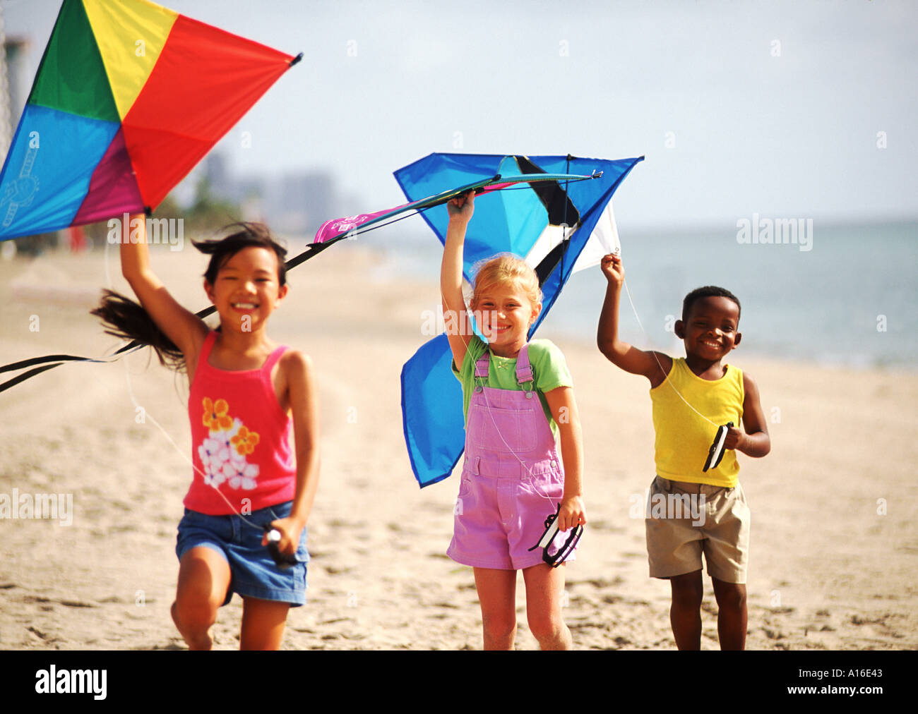 Children age 6 flying kites on the beach with mixed ethnic kids Stock