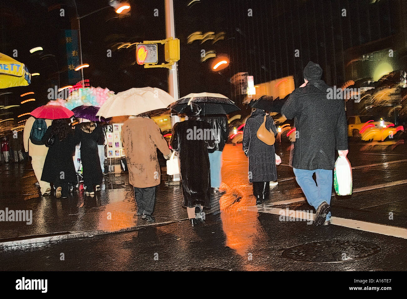 people walking in the rain at night in New York City holding umbrellas crossing the street Stock Photo