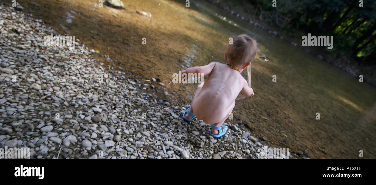 Little naked boy playing at the river bank Stock Photo - Ala