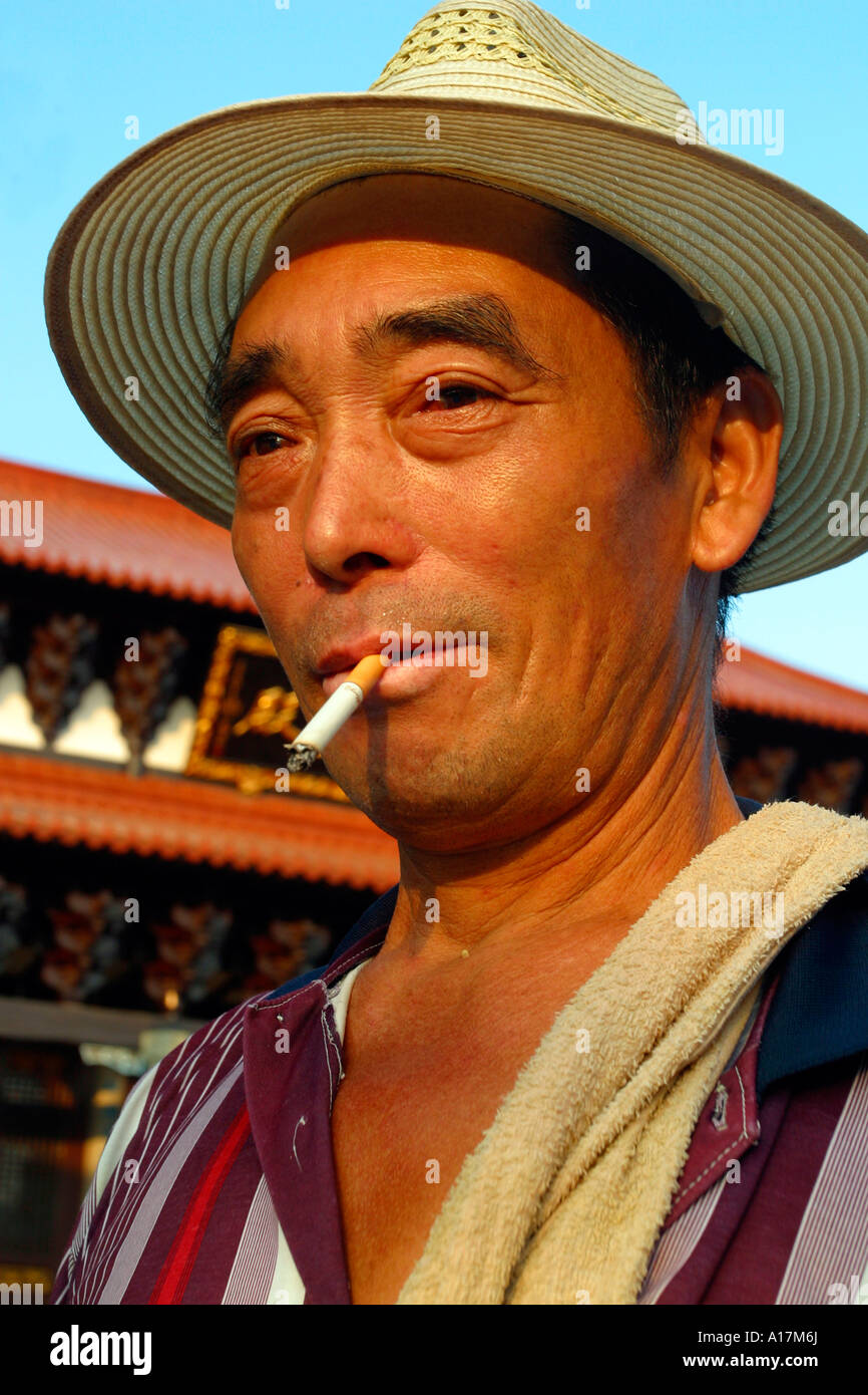 A Happy Chinese Man smiles as he smokes a cigarette. Stock Photo